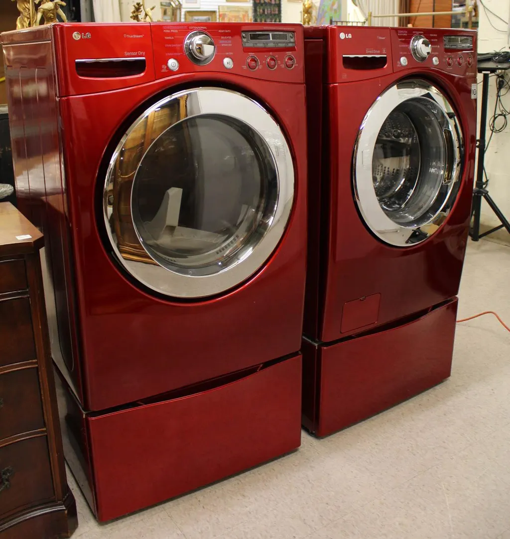 Two red front-loading washers next to a wooden dresser.