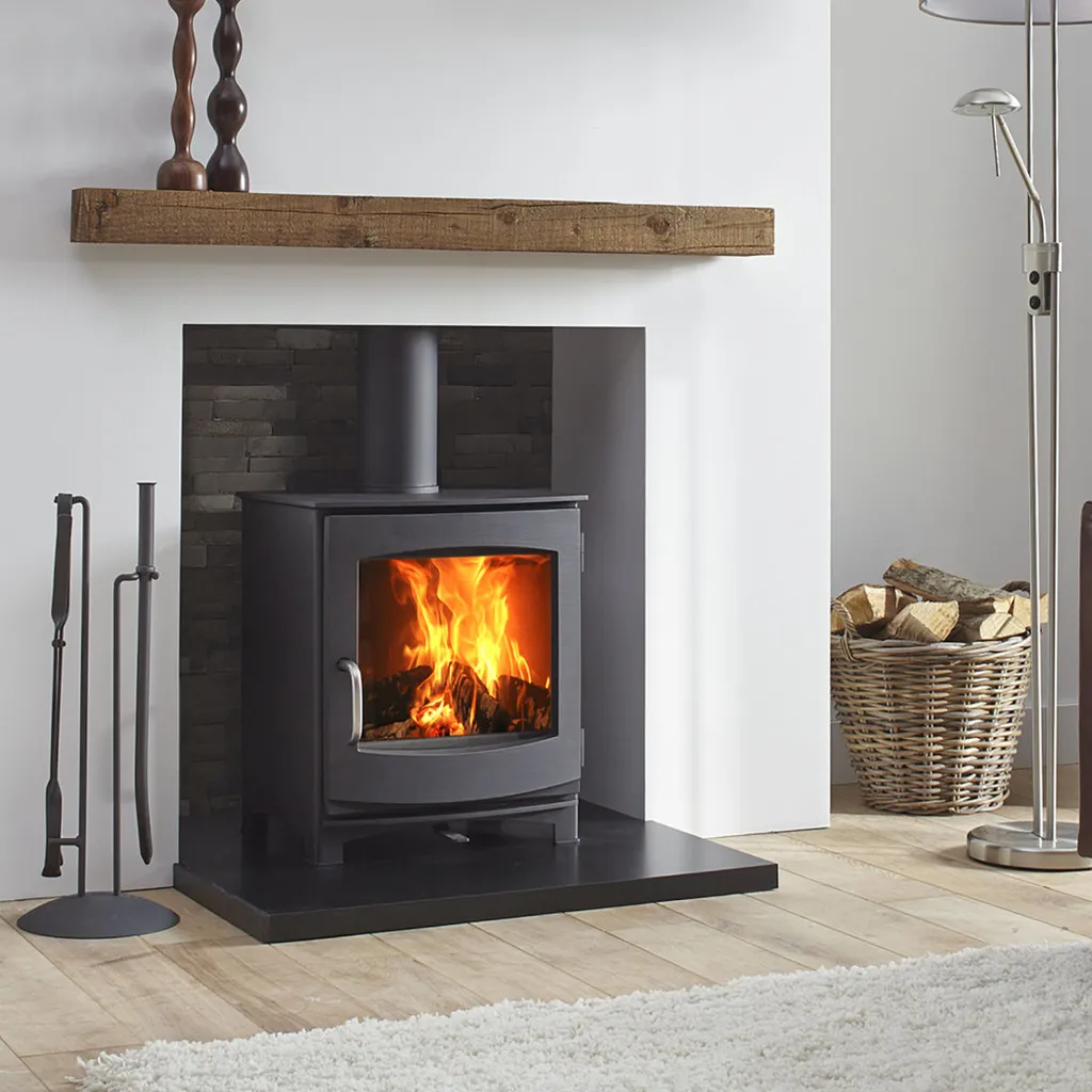 A wood-burning stove with a fire burning inside, a wooden shelf above, and a basket of logs.